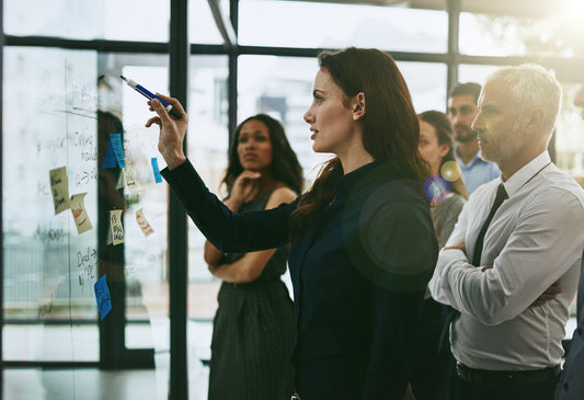 A group of professionals participating in a Lean Six Sigma Green Belt training session, standing and brainstorming on a glass wall with markers and stickers.